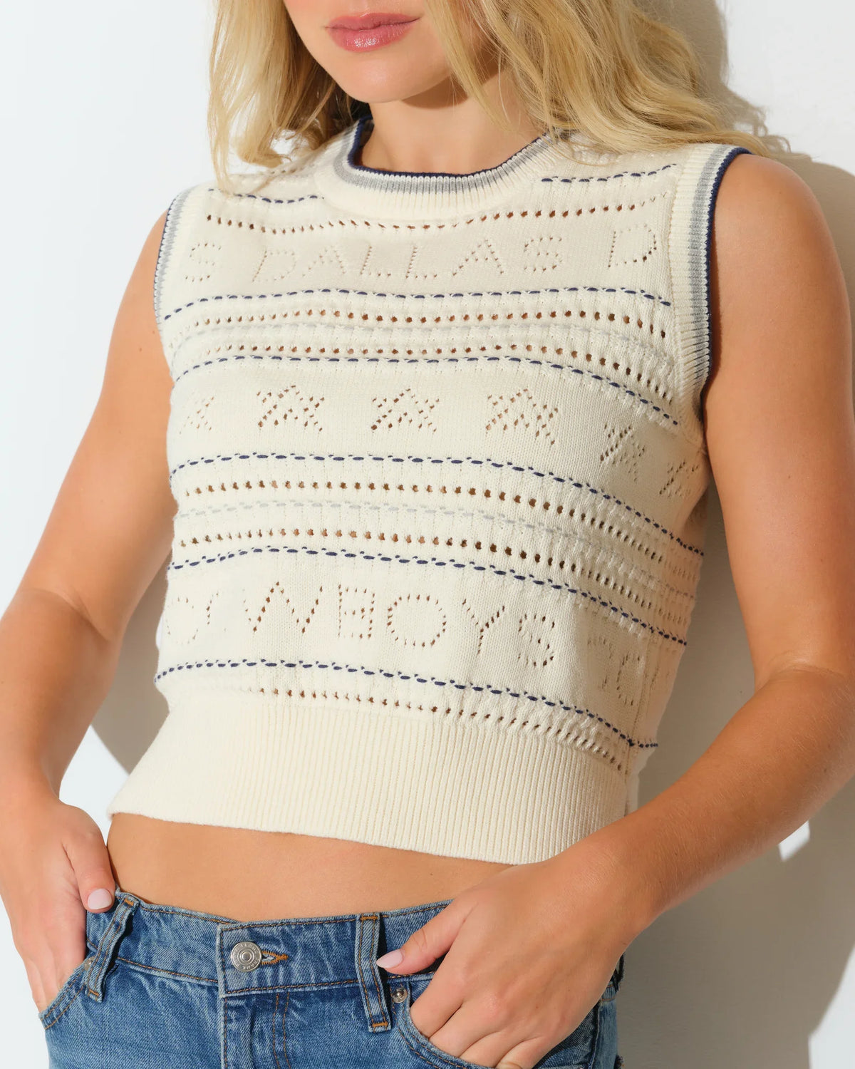 Ivory Dallas Cowboys cropped sweater vest with open-knit pattern and embroidered team lettering, styled with blue jeans.
