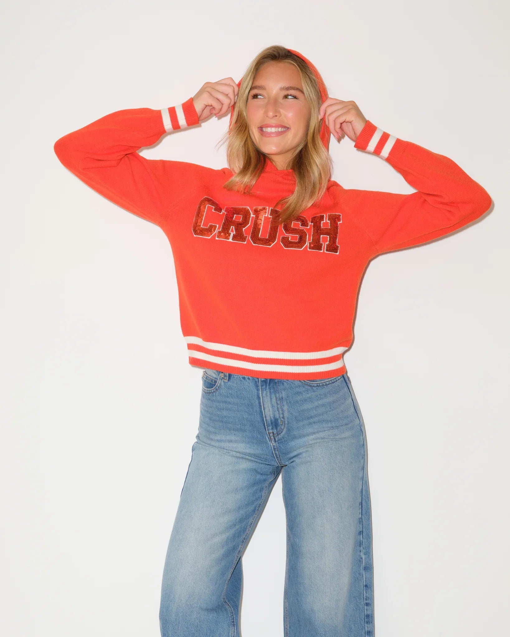 Red sequin knit hoodie with bold "CRUSH" lettering across the chest and white stripe trim at the hem.